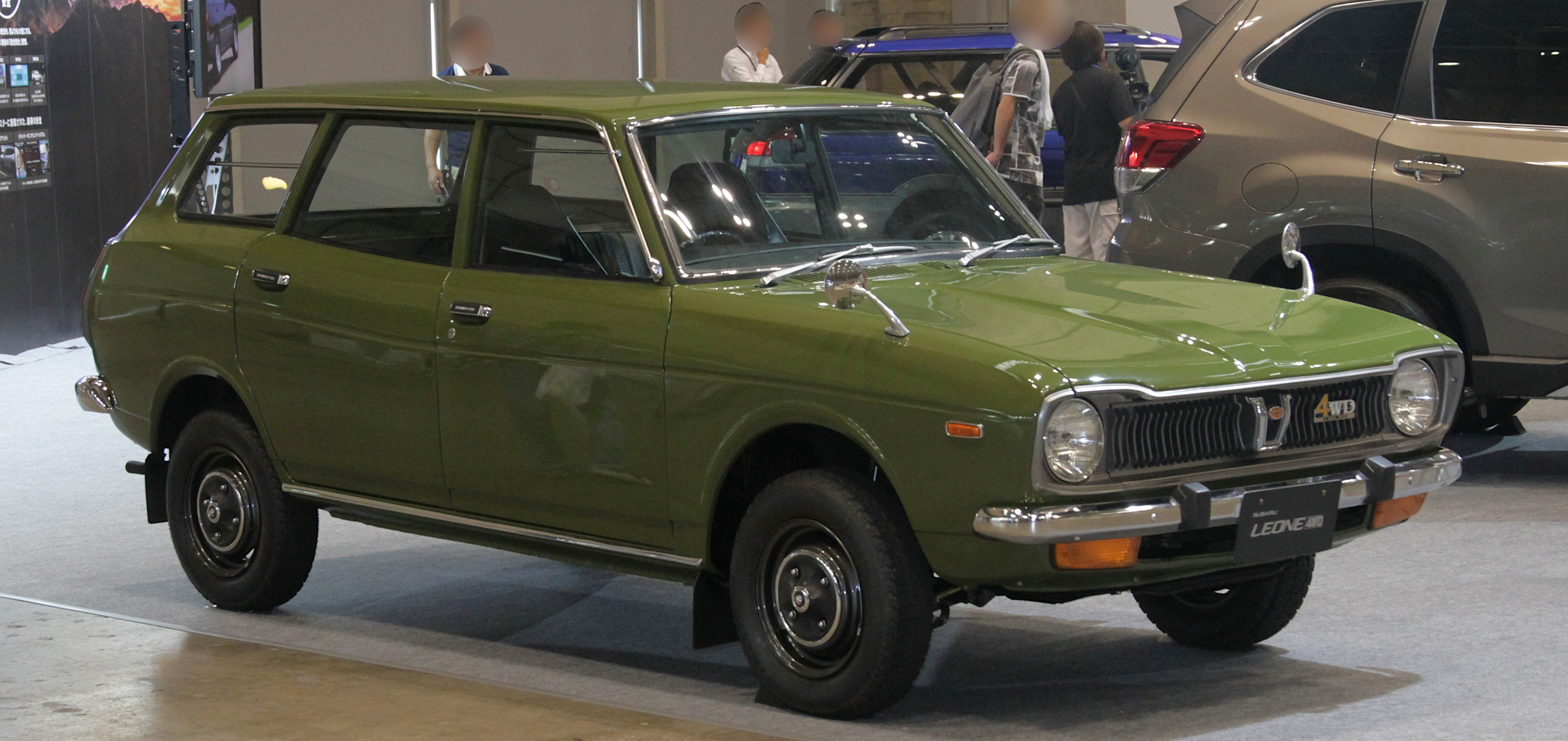 1972-style Subaru Leone 4WD Estate Van, green, front 3/4, "LEONE 4WD" badge/placard visible, Japanese display event